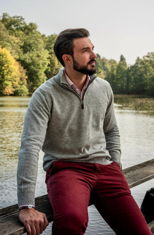 homme avec pull gris pantalon rouge assis sur une poutre le long d'une rivière